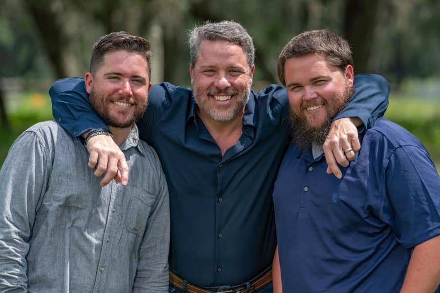 Joshua Purvis with his dad, Mark, and his brother Jake, arms around each other outdoors